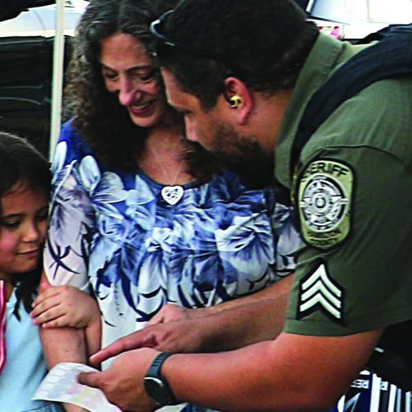  At last Tuesday’s National Night Out, HCSO Sgt. Pollard instructs a young attendee and her mother on how to kick off their sticker scavenger hunt.