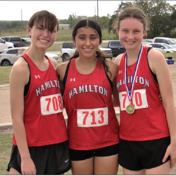 After placing fourth as a team in the district cross-country meet, varsity runners Berlin Bolton (left), Milagros Moncada and Chaska Downs celebrate Downs’ first-place finish and district crown. Photo by Jennifer Bolton