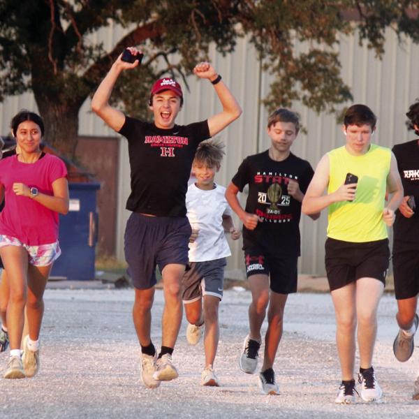 Sophomore Elijah Looke, joined by senior Milagros Moncada to his right, enthusiastically leads a pack of Hamilton High School cross country runners on their first official practice trek of the 2026 season at daybreak Monday morning. Moncada and the Lady Bulldogs captured Hamilton’s fourth consecutive and tenth all-time state crown last season, and after four consecutive trips to state from 2020 to 2023, the Bulldogs will be aiming to end a two-year drought with a stately return.