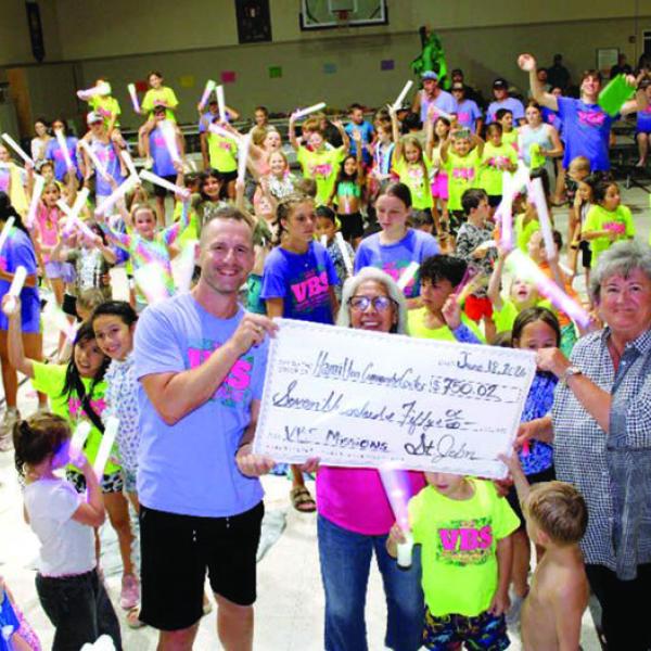 BIBLE SCHOOL BOOST: Following a theme of Rainforest Falls, St. John Lutheran Church Vacation Bible School explored the nature of God last week and concluded three days of VBS by presenting the Hamilton Community Center with a mission offering of $750.02. Pictured, l-r, Pastor Aaron Kalbas presents the offering to HCC officers Grace Powell and Michele Jones with help from enthusiastic explorers. Courtesy photo