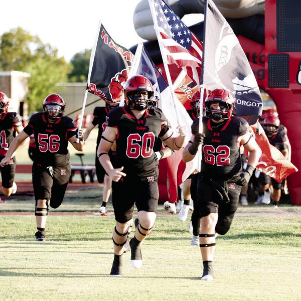 HOME OPENER: The Bulldogs had their first home game of their title defense 2026 season. Julian Ruiz (#56) Vanden Phillips (#60) and Zeb Murphee (#62) shoot out the “Dogpound” with flags to fire up the crowd and let them know the Bulldogs have arrived. Photo by Tracy Cox