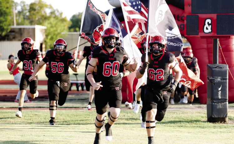 HOME OPENER: The Bulldogs had their first home game of their title defense 2026 season. Julian Ruiz (#56) Vanden Phillips (#60) and Zeb Murphee (#62) shoot out the “Dogpound” with flags to fire up the crowd and let them know the Bulldogs have arrived. Photo by Tracy Cox